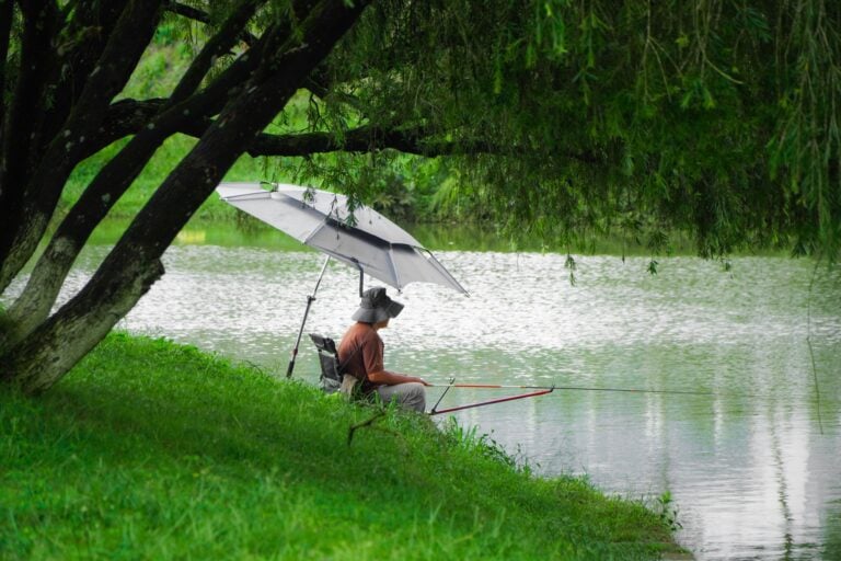 Ribolovac peca pod suncobranom uz jezero tijekom vrućeg dana